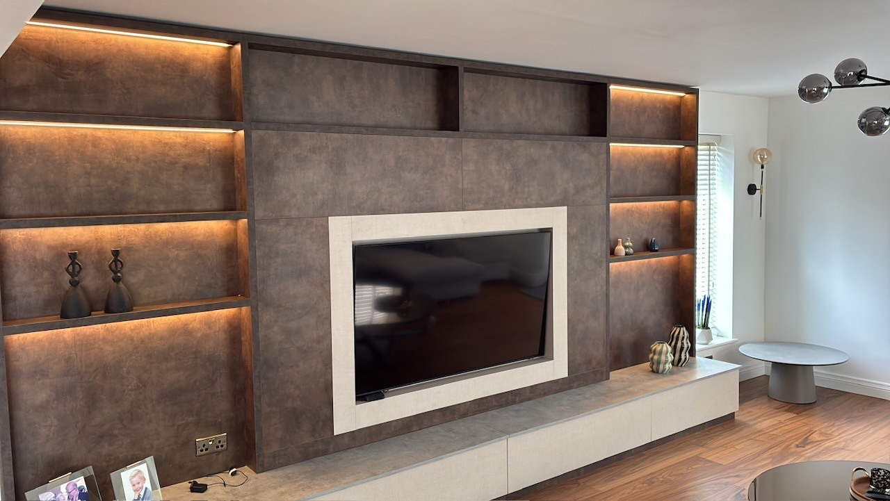 Bespoke lounge media wall with LED-lit shelving and TV in stone surround, Westby, Lytham — Wilsons Systems